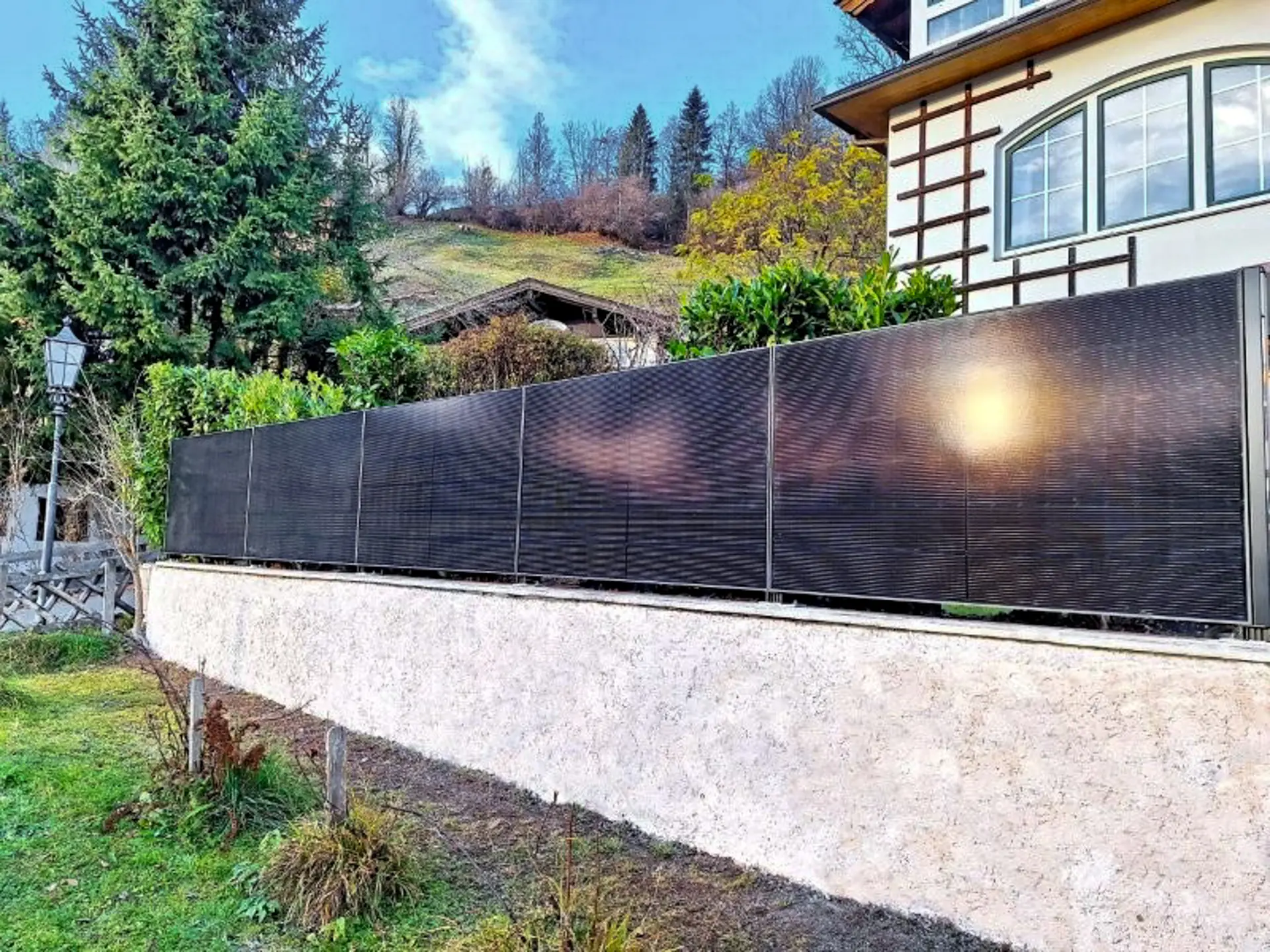 Solarzaun auf einer Gartenmauer, Sonne spiegelt sich in den Modulen
